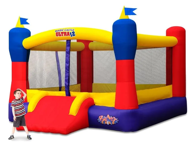 Blast Zone Magic Castle Ultra12 in yellow, red, blue and purple with flag-topped turrets and a red slide, a boy standing beside it