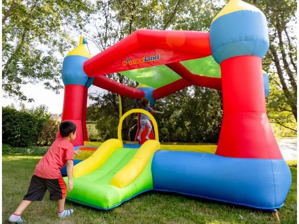 A boy climbing onto the slide of a Bounceland Party Castle on a shady lawn