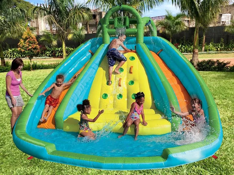 Children climbing the yellow rock wall and splashing down both slides of a Little Tikes Rocky Mountain River Race into its pool, a parent watching on a lawn